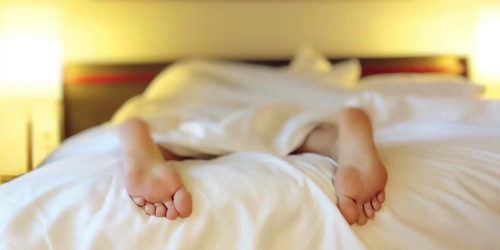 A person relaxing on a bed with feet under white sheets, conveying serenity.